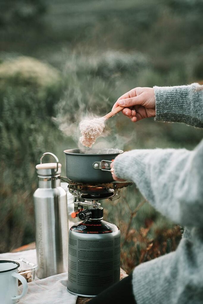 A person cooking a meal over a camping stove.