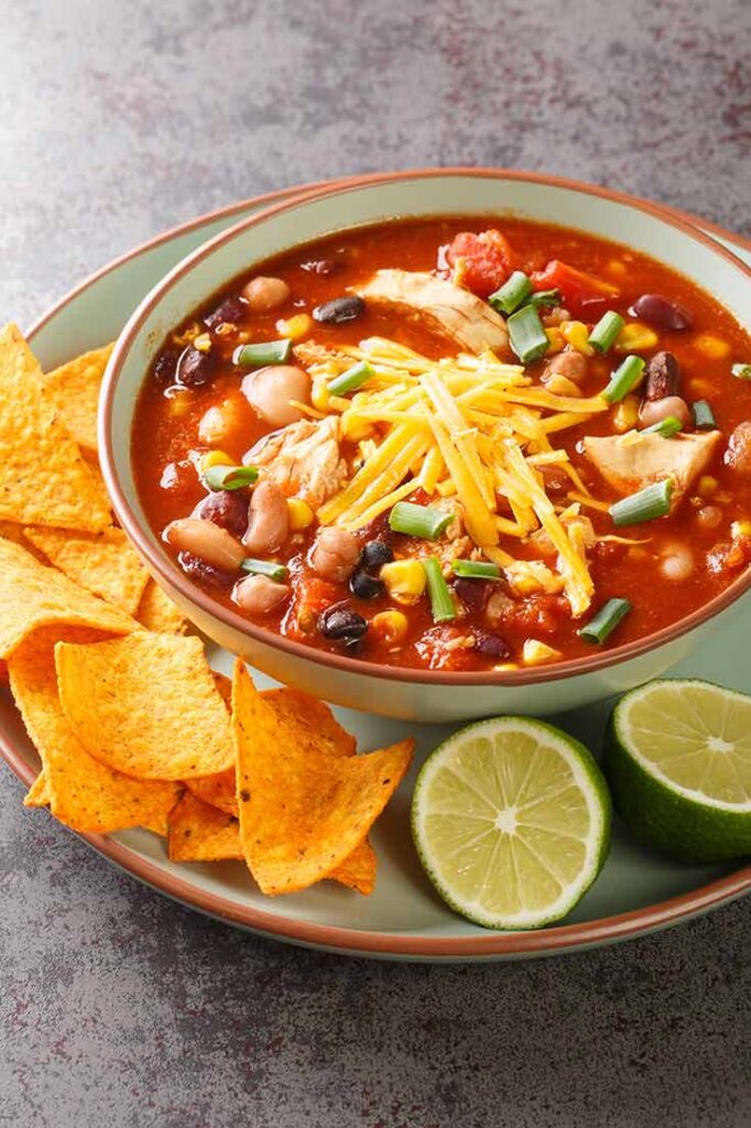 A bowl of chicken tortilla soup on a plate with some corn chops and limes on the side.