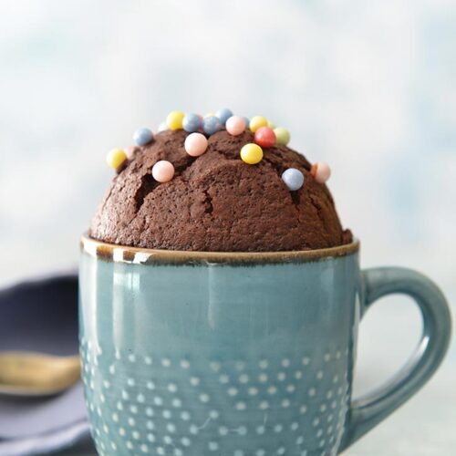 A single chocolate mug cake in a blue mug, topped with large sugar balls.