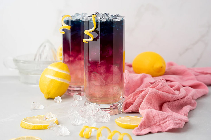 Two glasses of color-changing lemonade on a white surface and background.