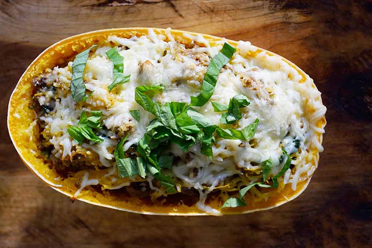 An overhead view of a half of a spaghetti squash stuffed and topped with melted cheese and fresh greens.