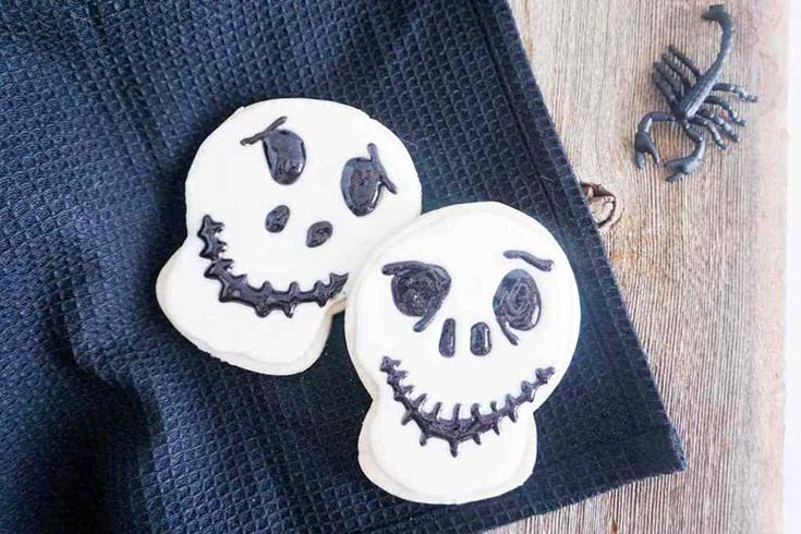 Two Jack Skellington cookies on a black towel.