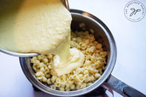 Pouring cheese sauce over cooked pasta shells.