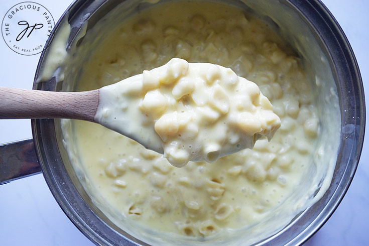 A spoon lifts some just-mixed Homemade Mac and Cheese out of a pot.