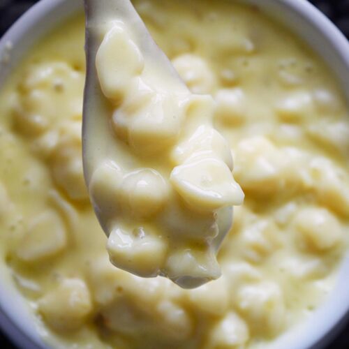 An overhead view of a wood spoon lifting some Homemade Mac and Cheese out of a white crock.