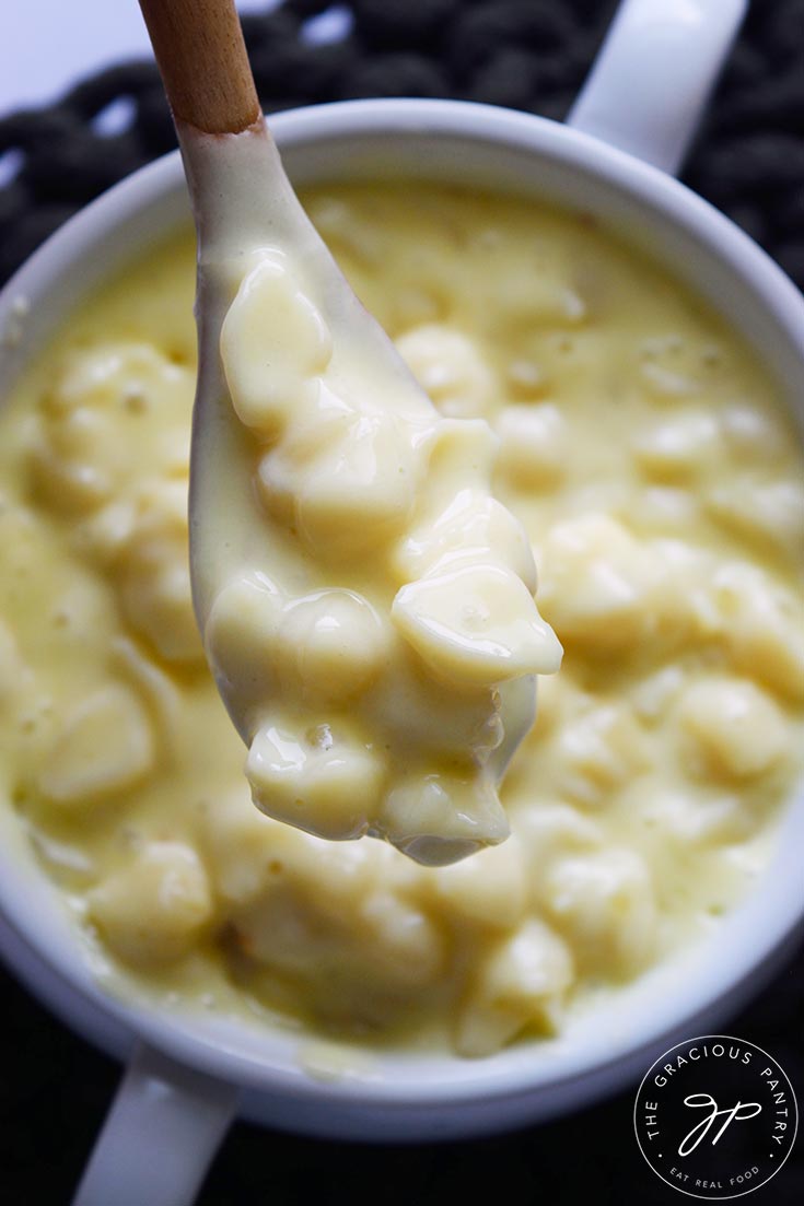 An overhead view of a wood spoon lifting some Homemade Mac and Cheese out of a white crock.