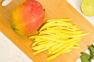 Sliced mango strips lay in a pile on a cutting board.