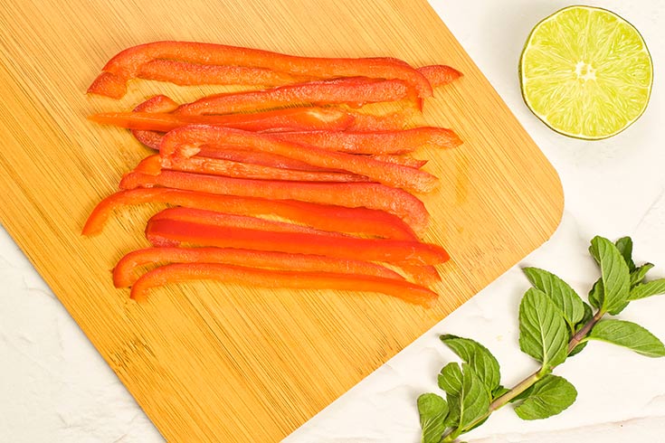 Red pepper strip lay in a pile on a cutting board.