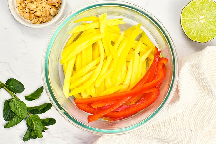 Sliced peppers added to a bowl of sliced mango.