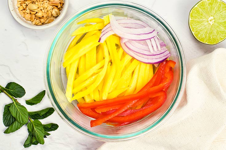 Onions added to mango and red bell peppers in a mixing bowl.