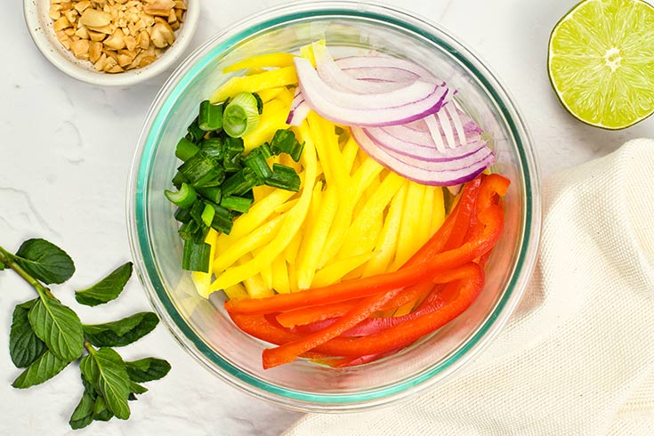 Green onions added to mango, bell peppers and red onion in a mixing bowl.