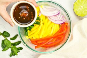 Dressing being poured over mango salad in a mixing bowl.