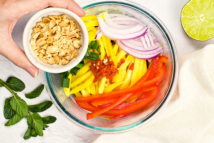 Peanut being added to mango salad in a mixing bowl.