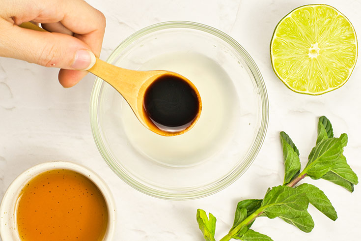 A spoon adds an ingredient to a glass bowl for making dressing.