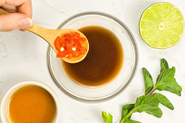 Chopped chili being added to a bowl of mixed dressing.