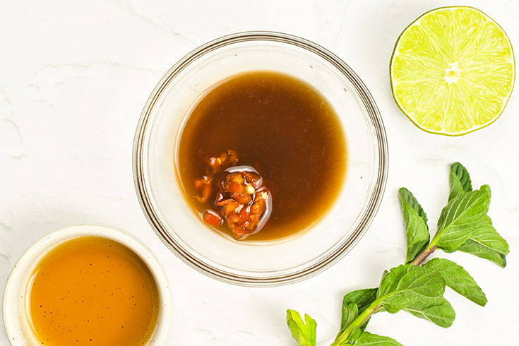 Chilis added to dressing in a glass bowl.