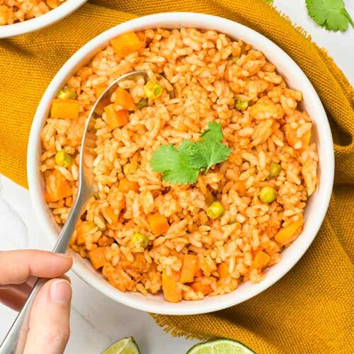 An overhead view of a spoon lifting some Mexican rice out of a white bowl.