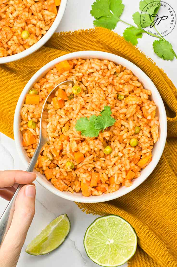 An overhead view of a spoon lifting some Mexican rice out of a white bowl.