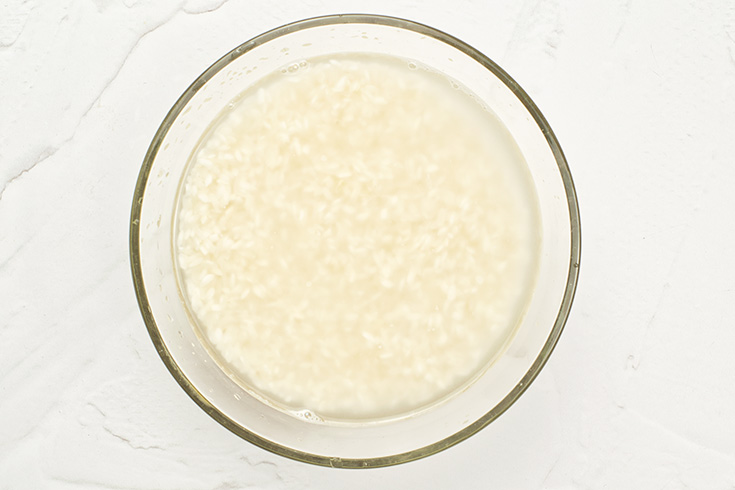 Rice soaking in some water in a glass bowl.