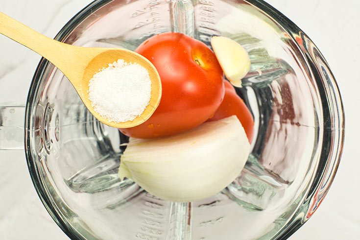 Adding salt to vegetables in a blender cup.