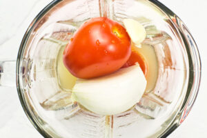 Adding broth to vegetables in a blender cup.