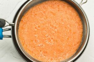 Blended veggies being strained through a strainer.