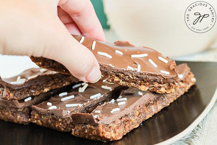 A hand reaches for a No Bake Pumpkin Protein Bar on a black plate.