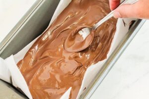 Spreading the melted chocolate over the bar based with a spoon.