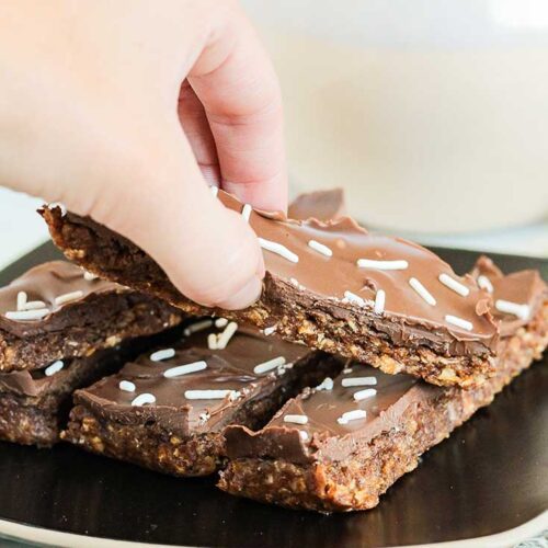 A hand reaches for a No Bake Pumpkin Protein Bar from a plate of them on a table.