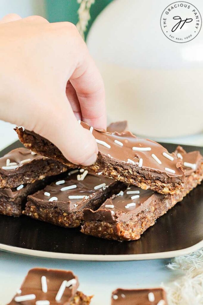 A hand reaches for a No Bake Pumpkin Protein Bar from a plate of them on a table.