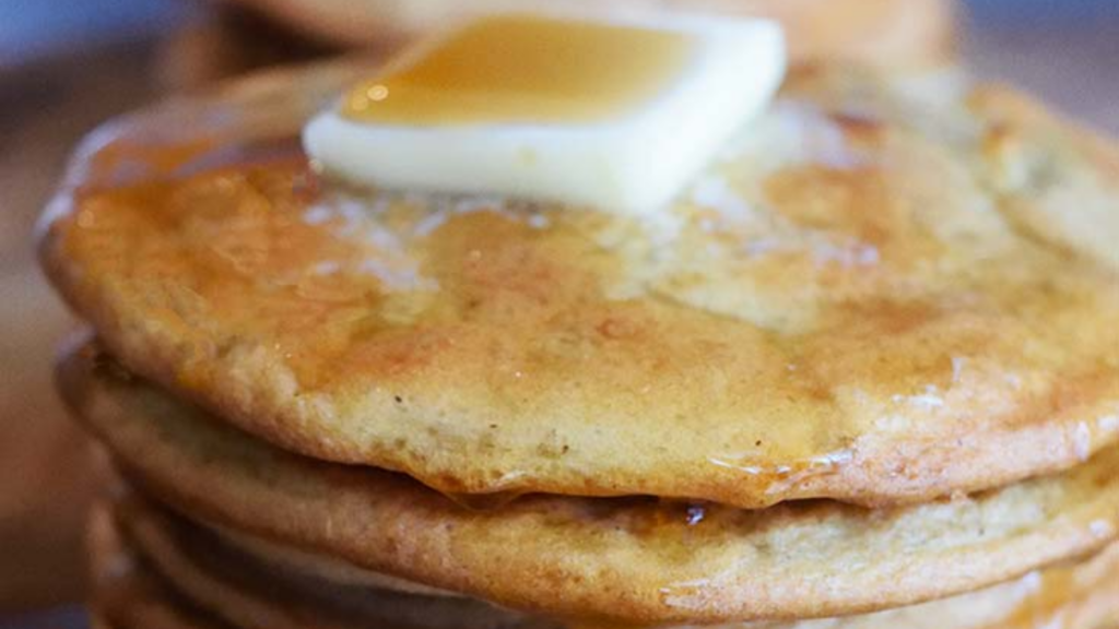 A closeup of a stack of pancakes with a pat of butter and syrup on top.