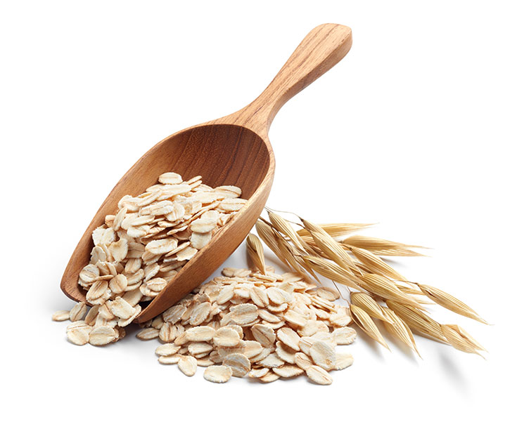 A wooden scoop sits filled with oats next to a pile of oats on a white background.