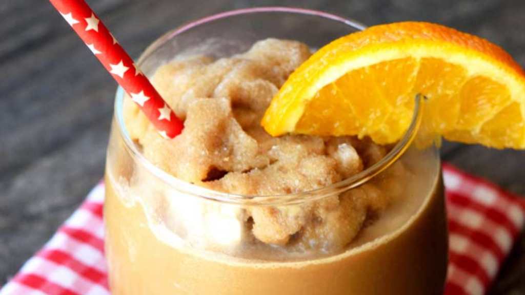 A close up of orange maple blended coffee in a clear glass with an orange wedge and straw for garnish.