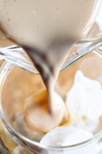 Front view of pouring Pumpkin Iced Coffee over ice in a cup.