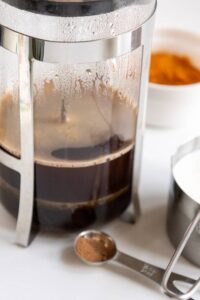 A french press brewing coffee on a white surface.