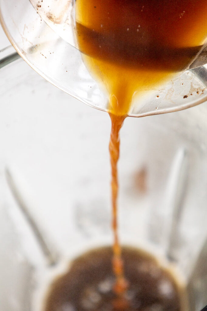 Pouring coffee from a french press into a blender cup.