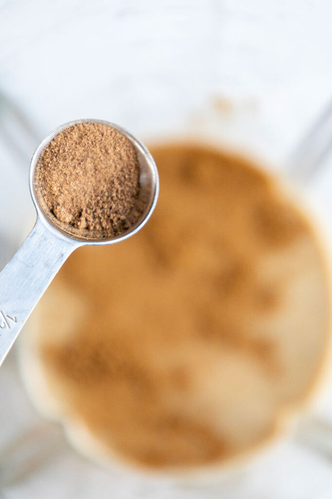 Adding spices to coffee and milk in a blender cup.