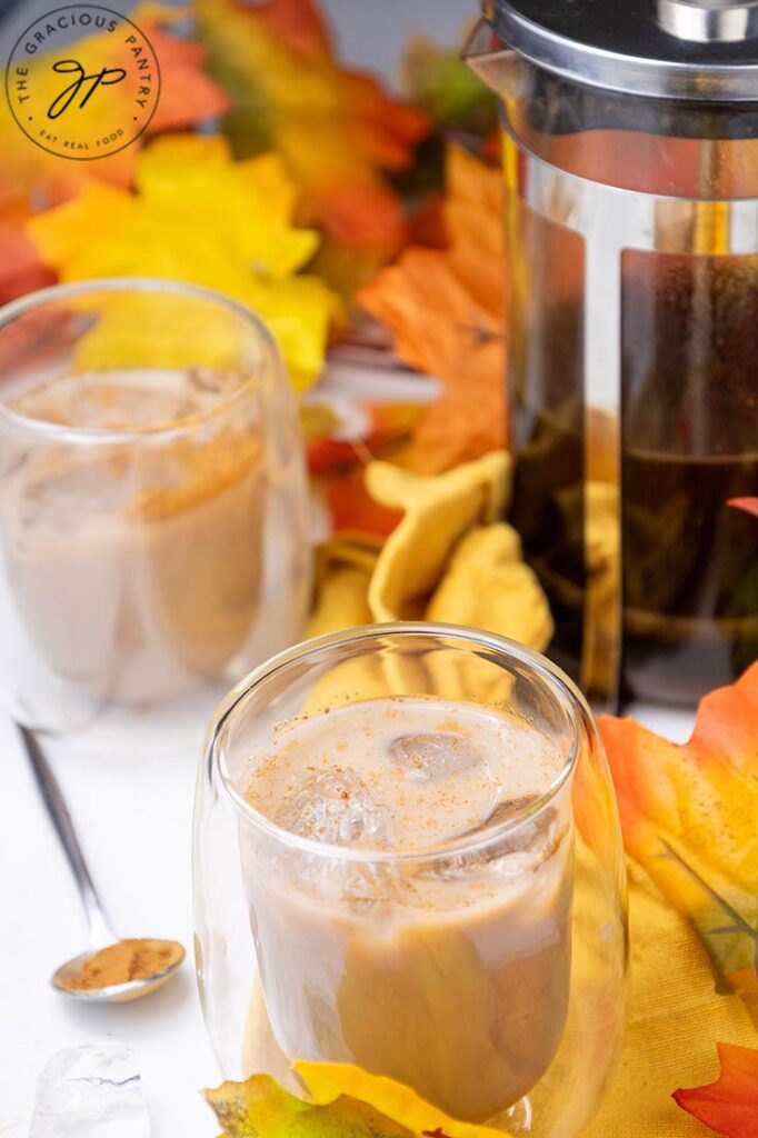 A side view of two cups filled with Pumpkin Iced Coffee sitting next to a french press with coffee in it.