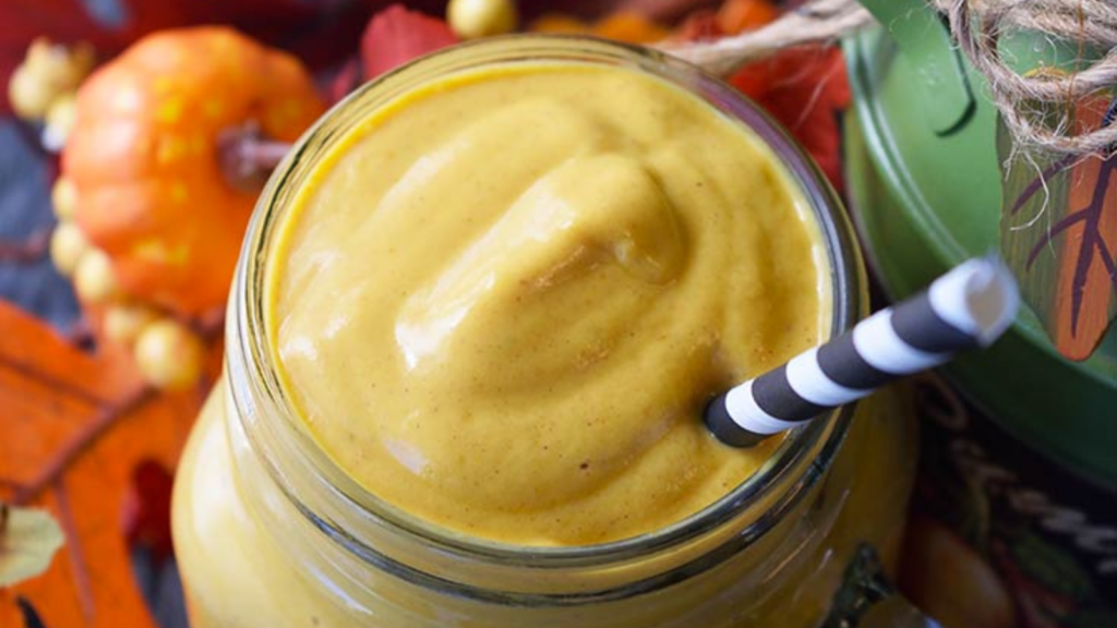 A closeup view of a glass jar filled with pumpkin pie smoothie. A straw sits in the drink.