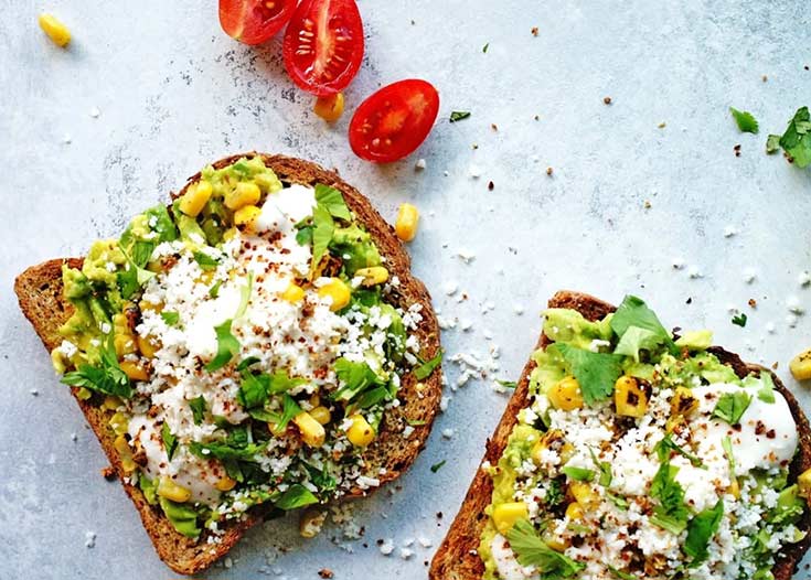 Two slices of street corn avocado toast on a white background.