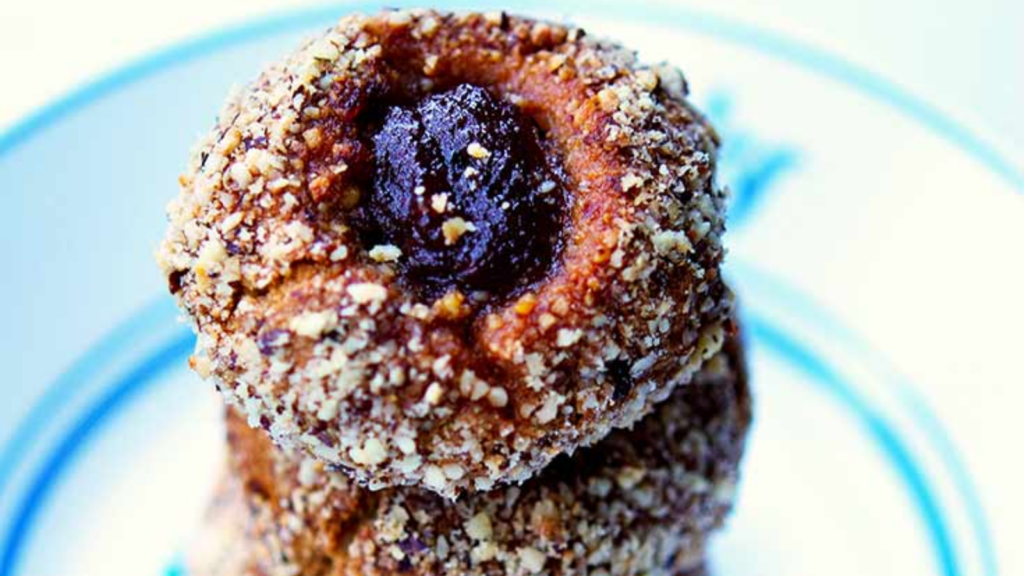 A closeup of a stack of thumbprint cookies with jam in the middle.