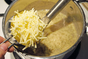 Adding cheese to white sauce in a pot.