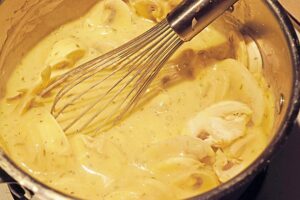 Stirring mushrooms into white sauce in a pot.