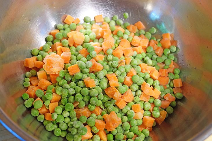 Frozen peas and carrots in a large mixing bowl.