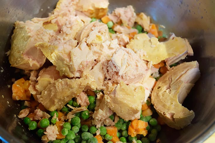 Tuna added to frozen veggies in a mixing bowl.