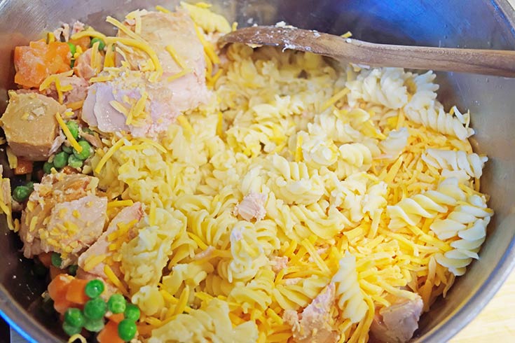 Cooked pasta added to tuna, veggies and cheese in a large mixing bowl.