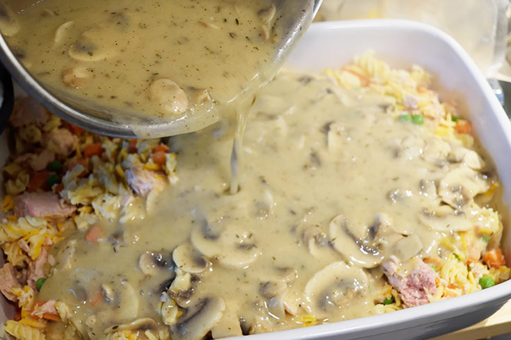 Pouring white sauce over the casserole filling in a casserole dish.