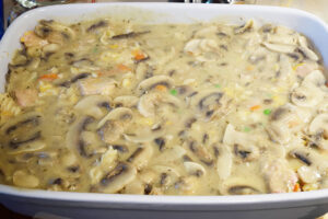 Sauce with mushrooms spread evenly over casserole filling in a white casserole dish.