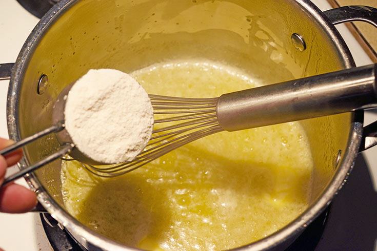 Adding flour to melted butter in a pot.