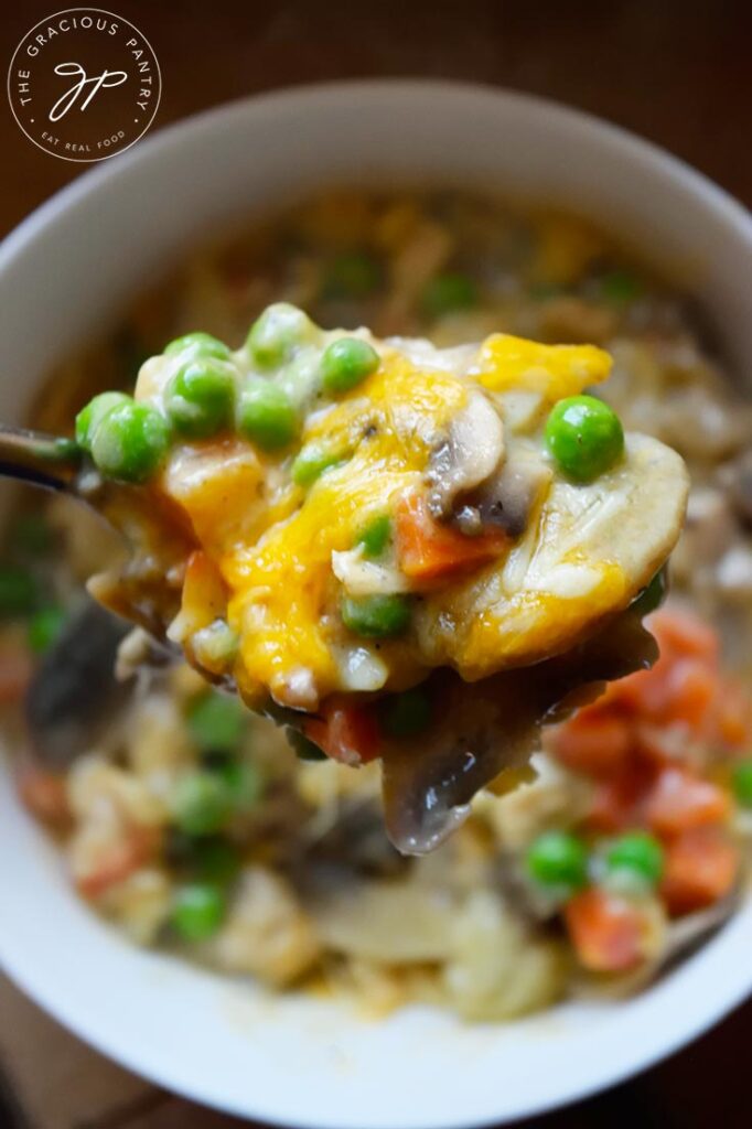 A spoon filled with Tuna Noodle Casserole lifts some of the dish out of a white bowl.